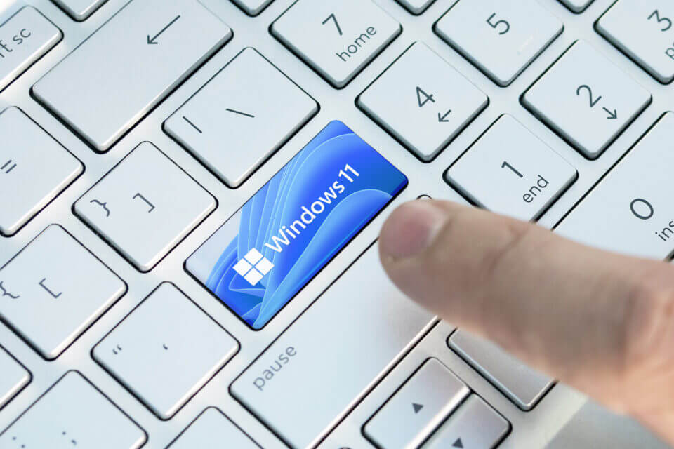 A finger prepares to press a Windows 11 key on a silver, white-key keyboard—signifying IT support and cyber security access.
