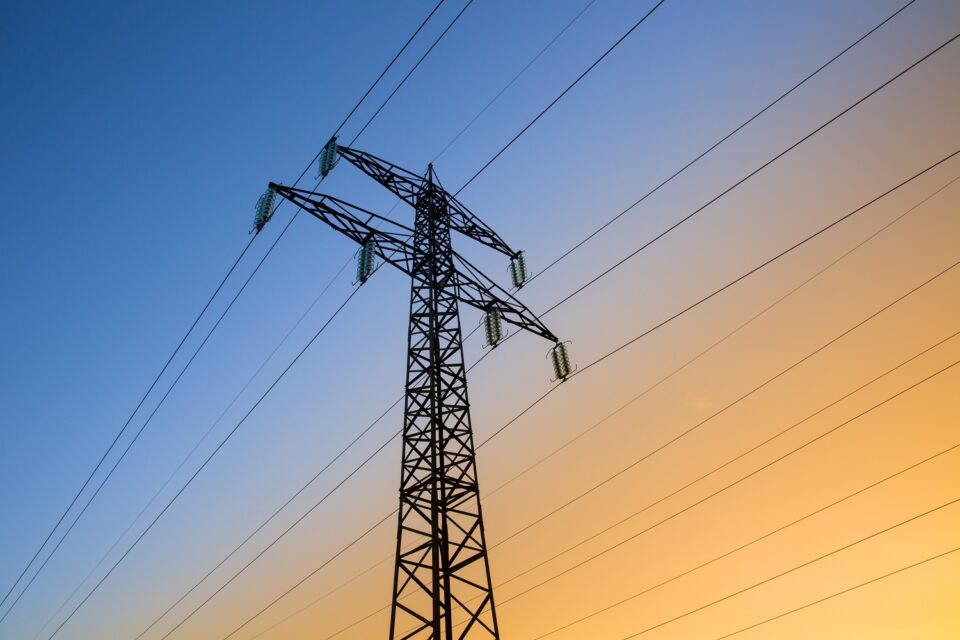 A tall transmission tower with power lines stands at sunset, symbolising secure, reliable, and connected digital infrastructure.