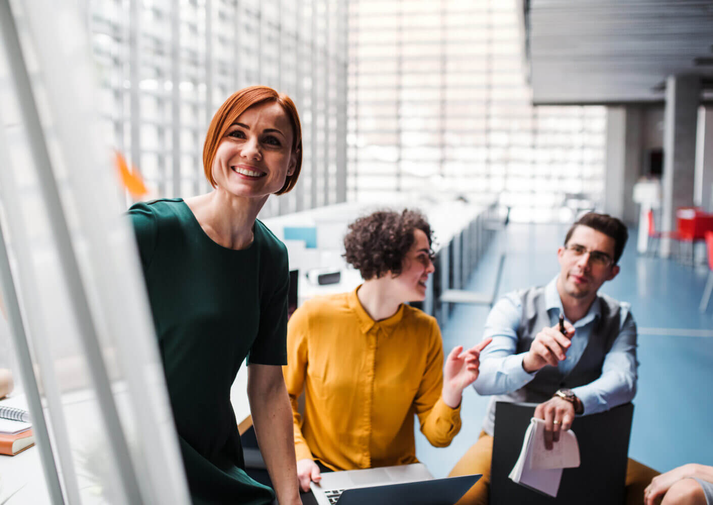 Three professionals discuss cybersecurity solutions by a whiteboard, with laptops open for IT support planning in a modern office.