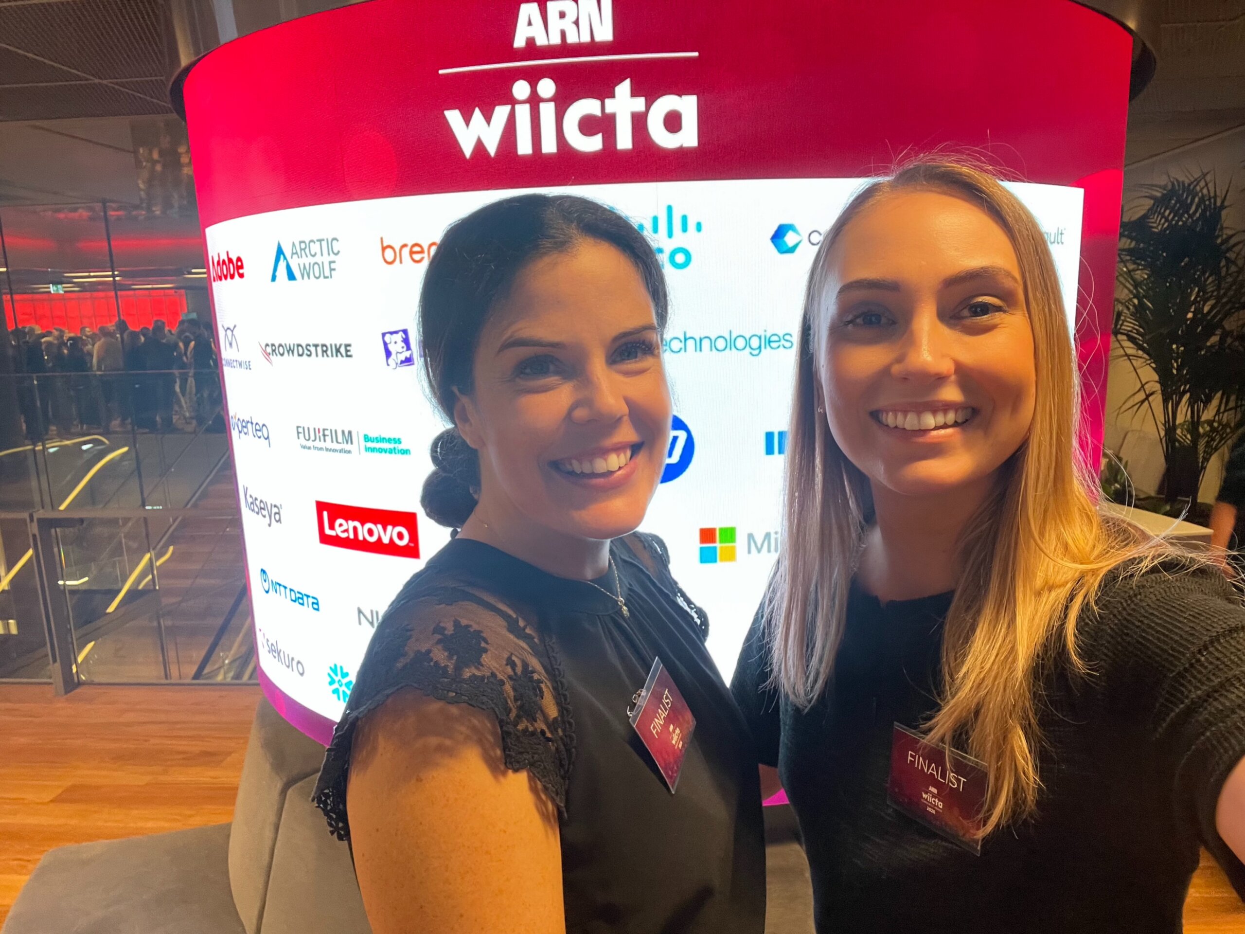 Megan Visser and Jessica Tolsma posing at the WIICTA 2026 event sponsor wall